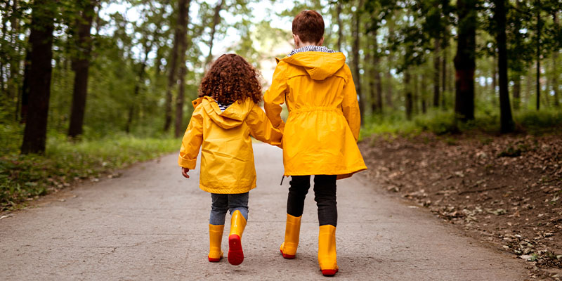 Siblings walking on path in yellow raincoats.